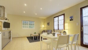 A modern kitchen with a built-in oven and microwave, a dining area with a white table and chairs, and a window with a view of the outdoors. - Gîte du Héron Gris (BOULIGNEUX)