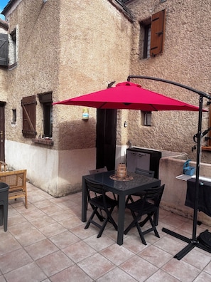 An outdoor patio with a table and chairs, a red umbrella, and a stone building in the background.