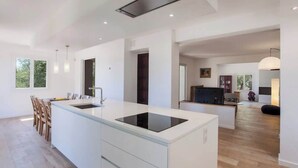 A modern kitchen with a central island, white cabinetry, and a black induction cooktop. - Villa Le Corps de Garde (Furiani)