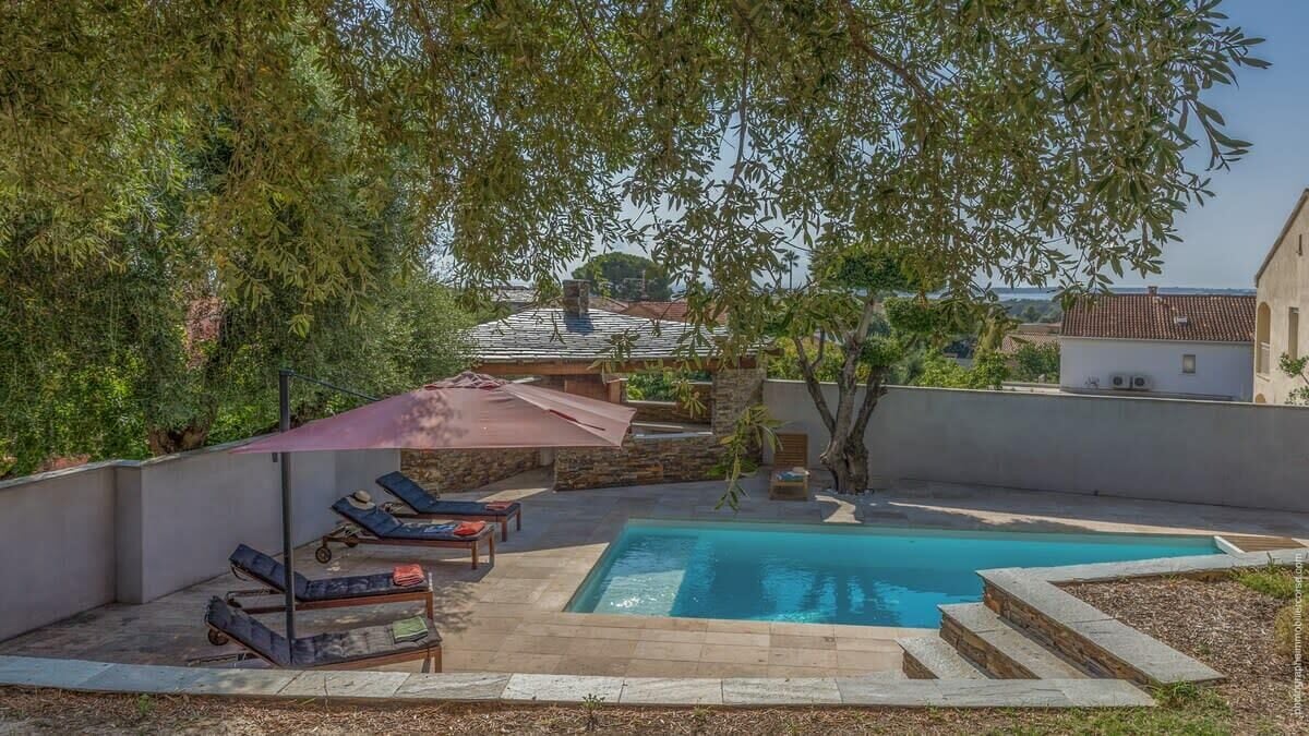 A backyard with a swimming pool, lounge chairs, and a pergola providing shade.