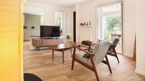 A modern living room with a flat-screen TV, wooden furniture, and a view of the outdoors. - Villa Le Corps de Garde (Furiani)