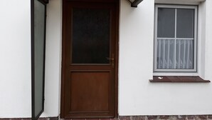 Eine Holztür mit Glasfenster, ein Fenster mit Vorhang und ein kleines Fensterbrett darunter.