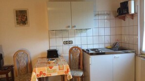 Eine kleine Küche mit weißen Schränken, einer gefliesten Spritzschutzwand, einer Arbeitsplatte und einem Esstisch mit Stühlen.