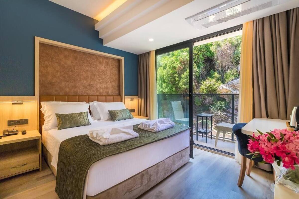 Ein Hotelzimmer mit Bett, Nachttischen, Schreibtisch und einem Balkon mit Blick auf Grünflächen.