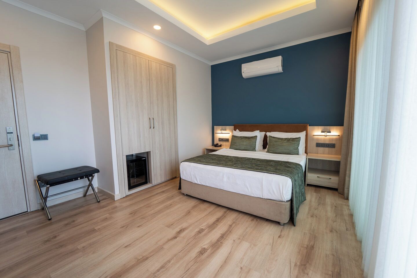 A modern bedroom with a bed, bedside tables, a bench, a wardrobe, and an air conditioning unit.