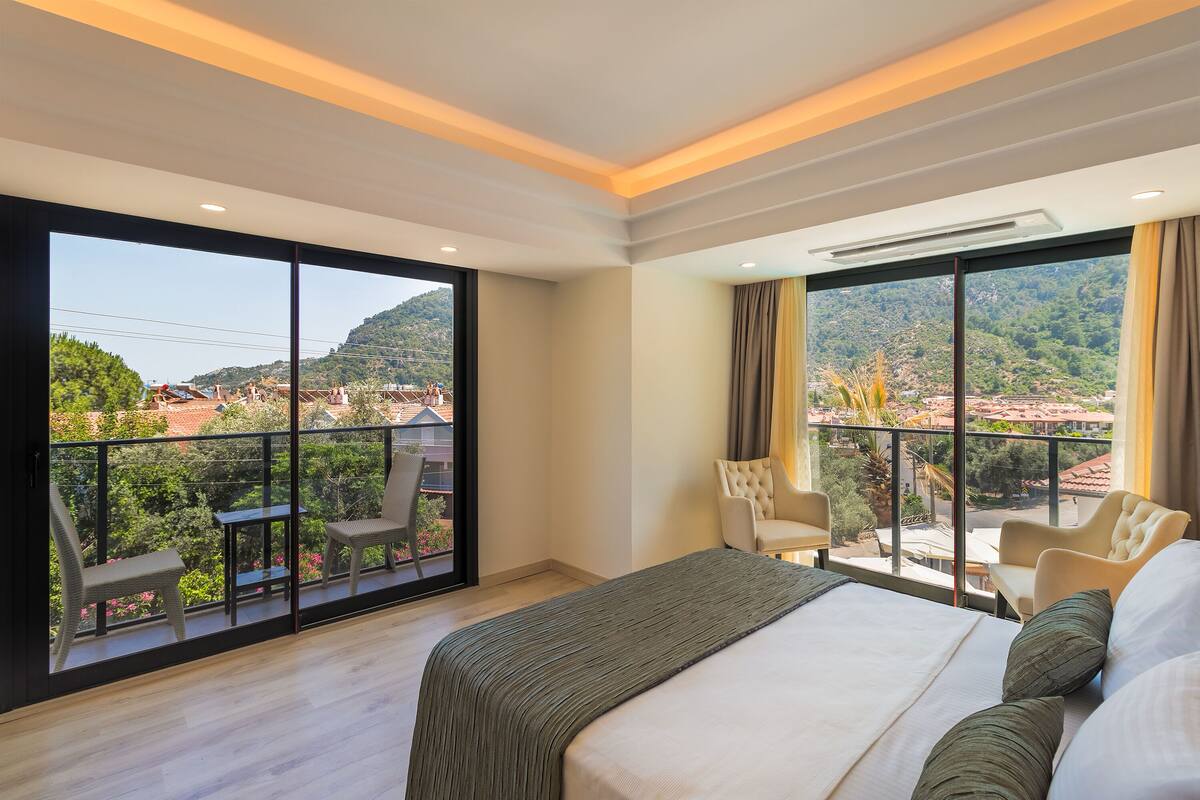 Ein Hotelzimmer mit einem großen Bett, einem Balkon mit Sitzgelegenheiten und Blick auf die umliegende Landschaft.