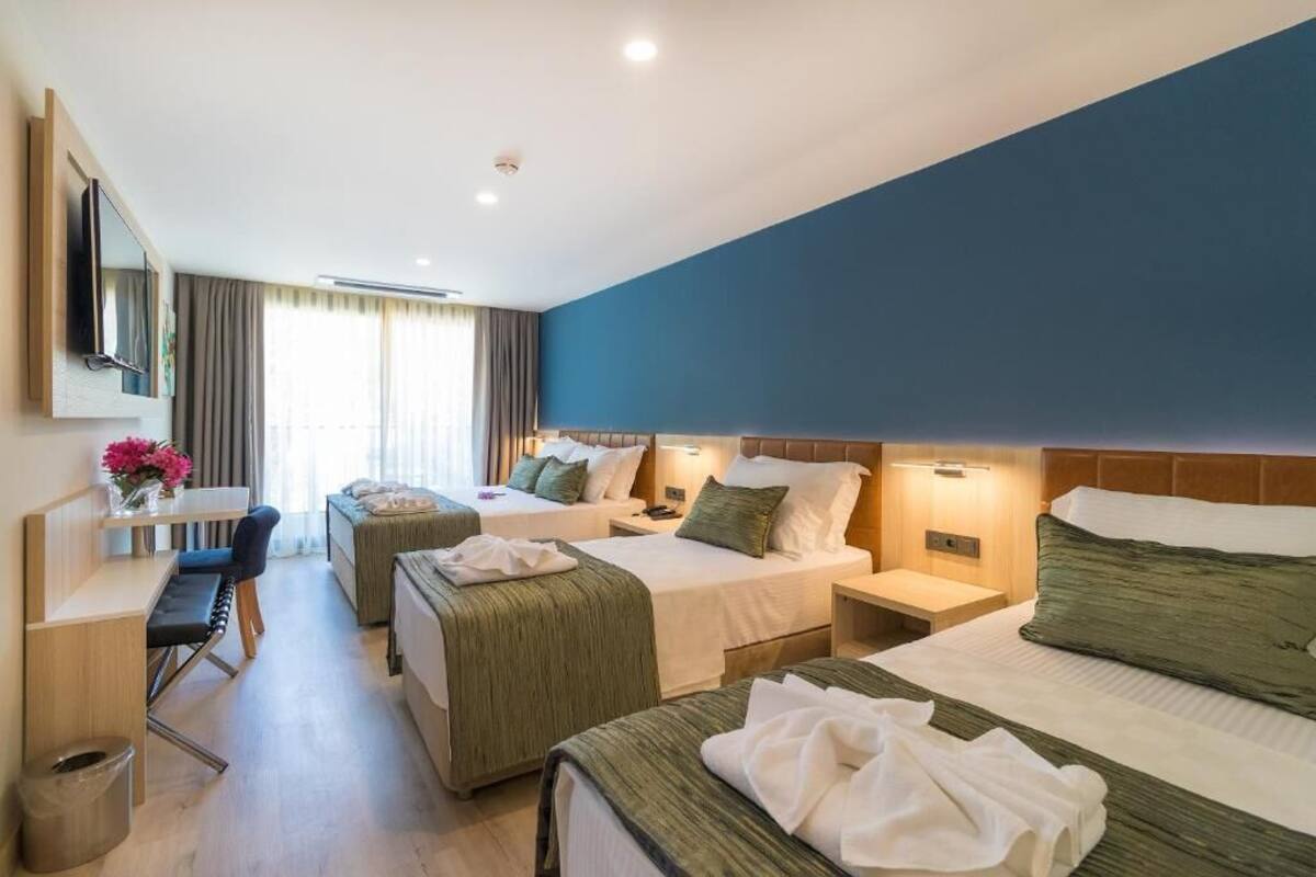 Ein Hotelzimmer mit zwei Betten, einem Schreibtisch, einem Stuhl, einem Fernseher und einem Fenster mit Vorhängen.
