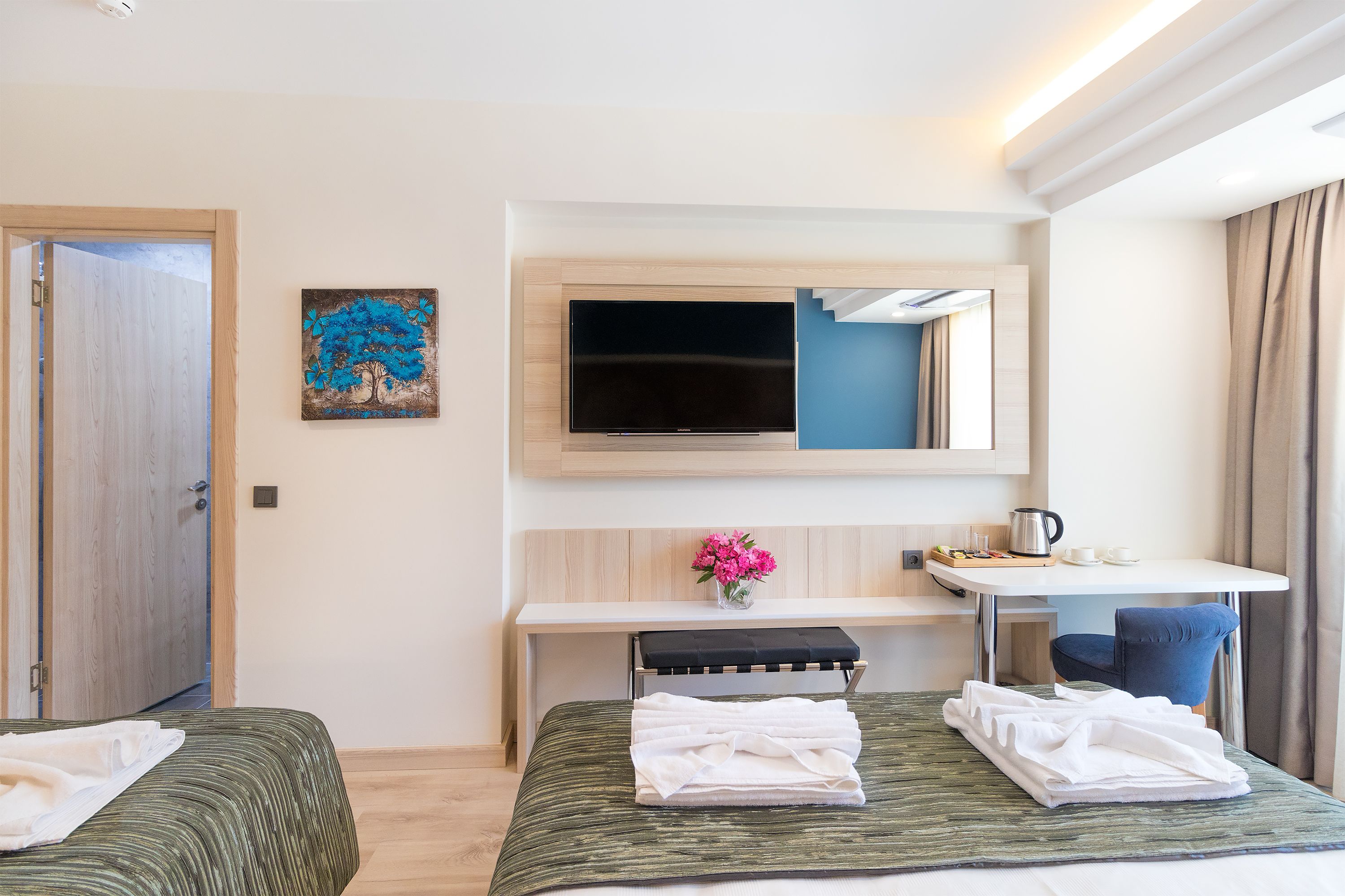 A hotel room with two beds, a desk, a television, and a painting on the wall.