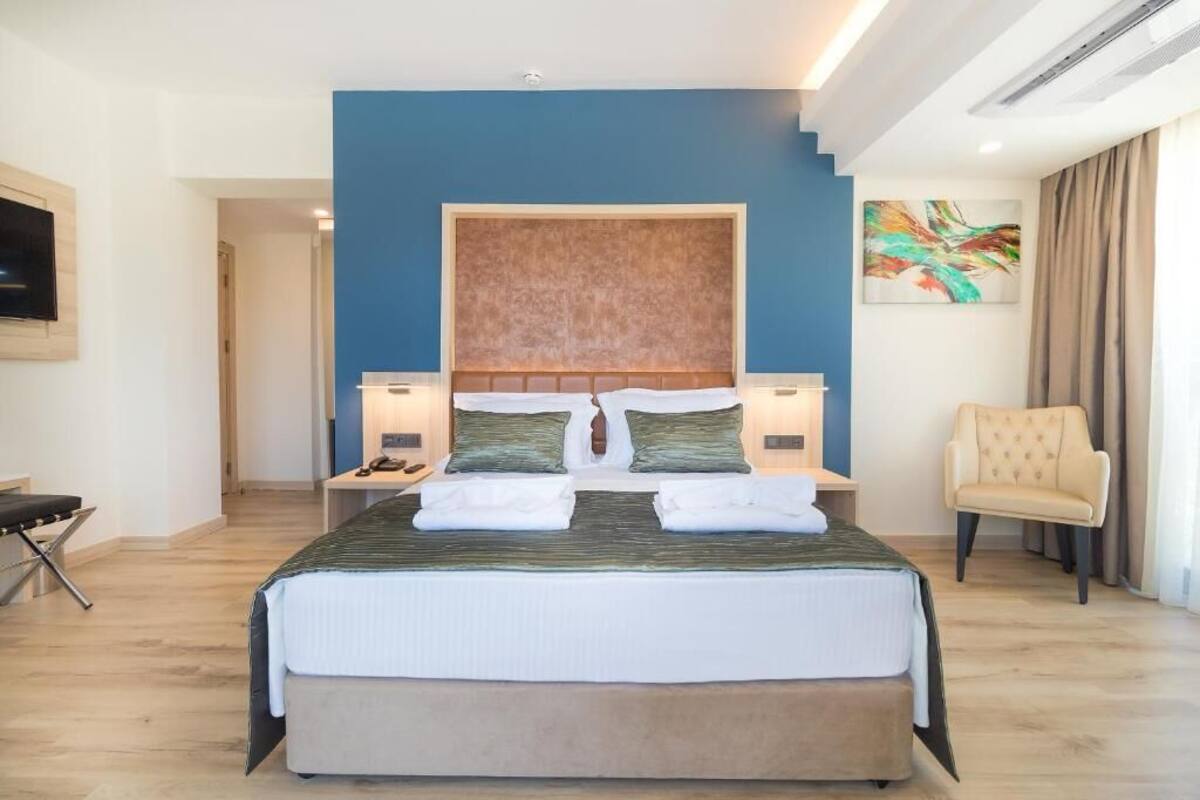 Ein Hotelzimmer mit einem großen Bett, einem Kopfteil, Nachttischen, einem Sessel und einem Bild an der Wand.