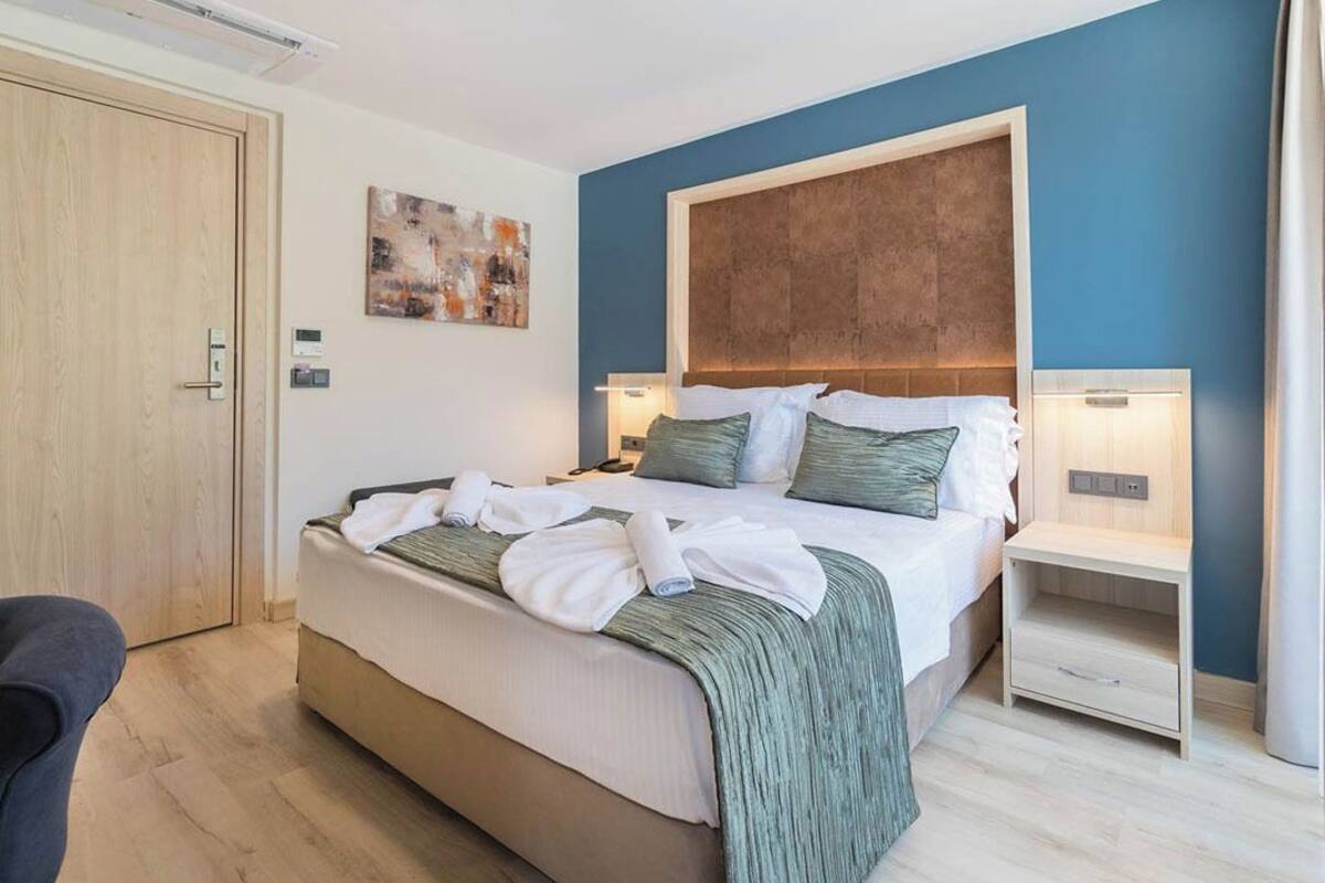 Ein Hotelzimmer mit einem großen Bett, einer Holztür, einem Bild an der Wand und einem Nachttisch mit einer Lampe.