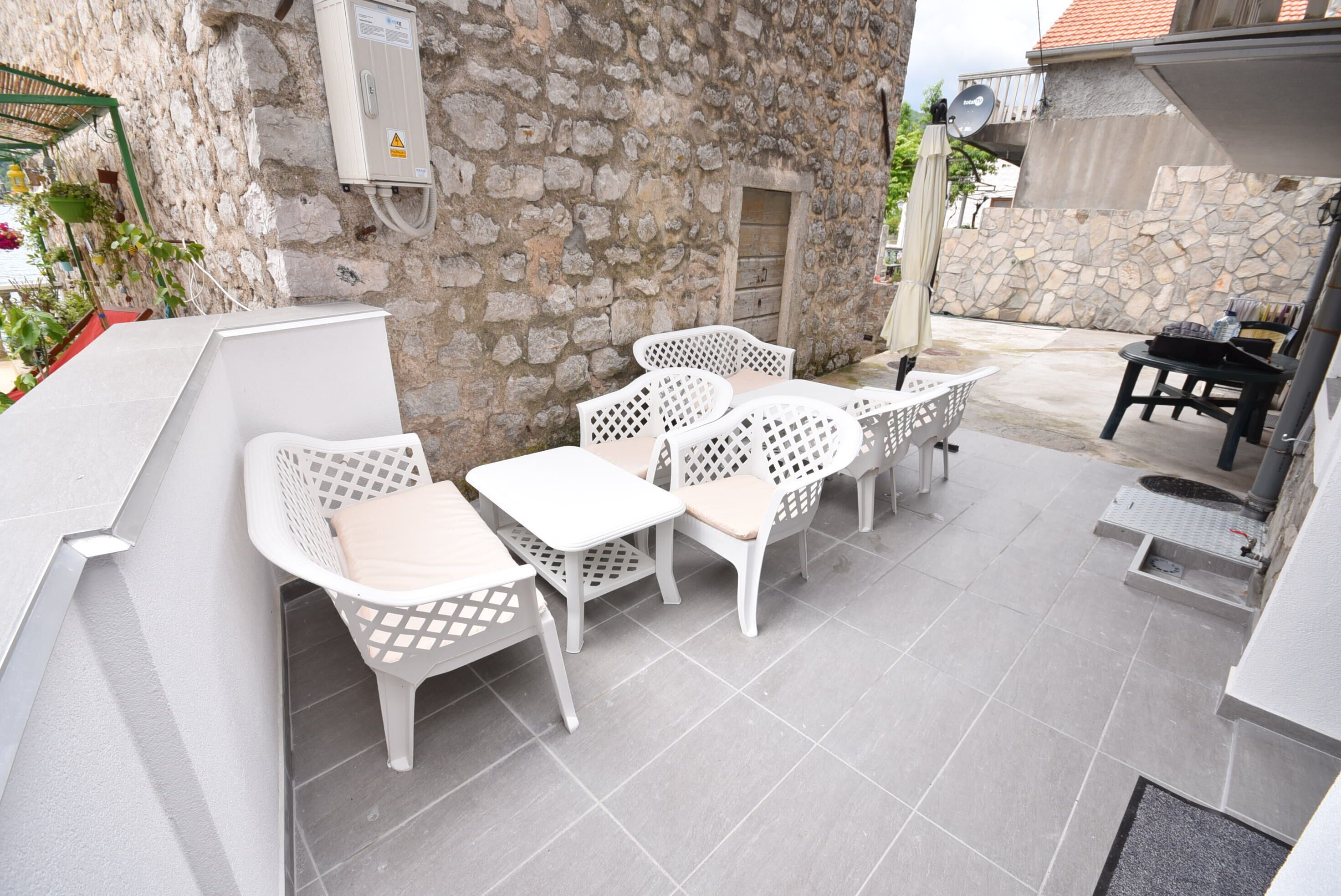 A patio area with white wicker furniture, a stone wall, and a satellite dish.