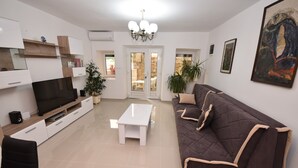 Een moderne woonkamer met een flatscreen televisie, een witte salontafel, een bruine bank en een kroonluchter.