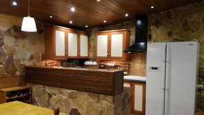 A kitchen with stone walls, wooden cabinets, a white refrigerator, and a wooden dining table with chairs. - Casa Axier-2 Villa with Private Pool - Air Conditioning (Accommodates 2–16 people) (Biar)