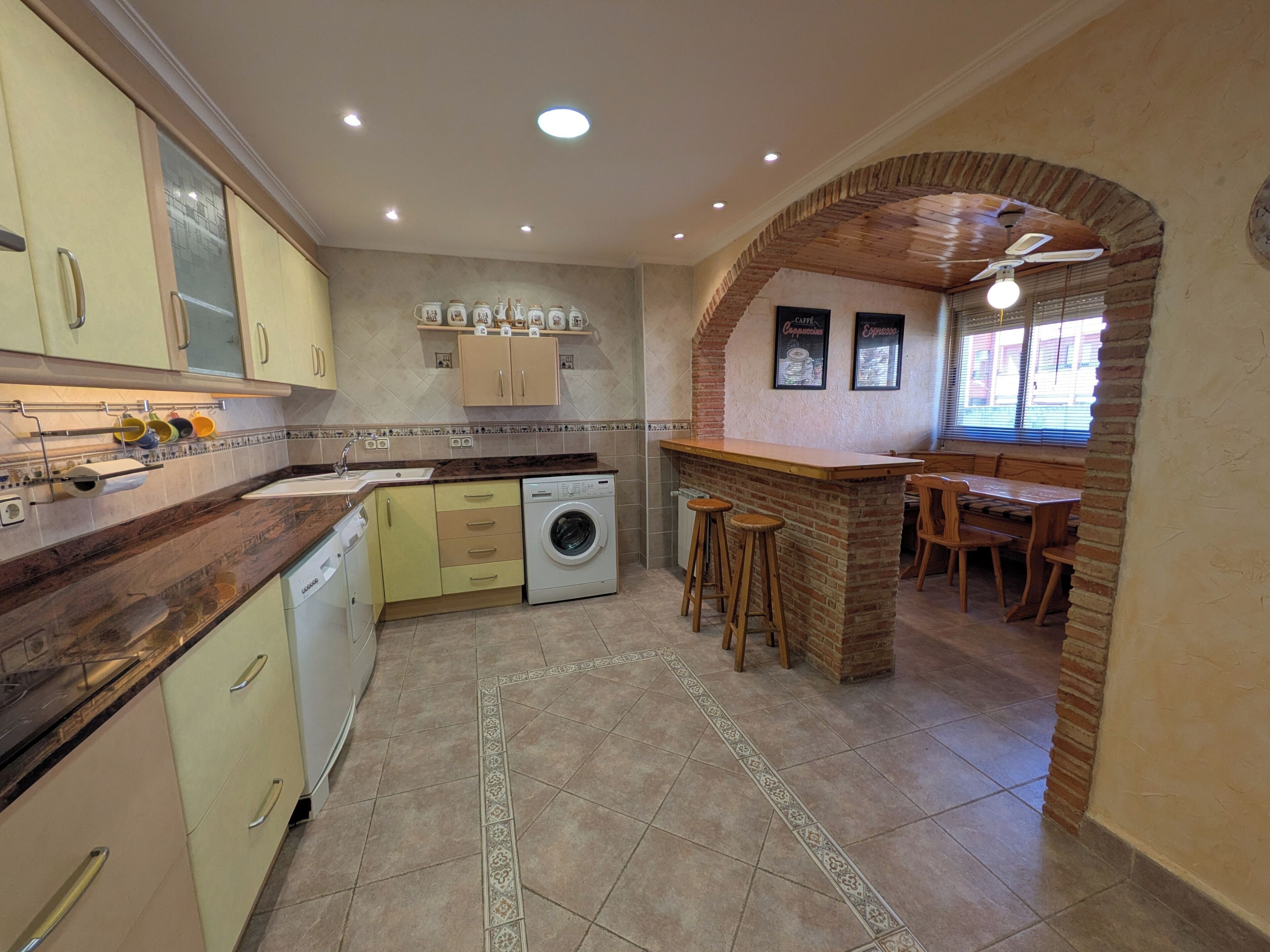 A kitchen with a washing machine, a coffee bar, and a dining area with a brick archway.