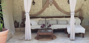Una cama con dosel y cuatro columnas, un tapiz tejido, una mesita y objetos decorativos.