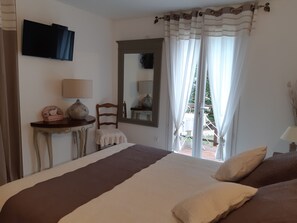 Un dormitorio con una cama, una mesita de noche con lámpara, una silla, un espejo y una ventana con cortinas.