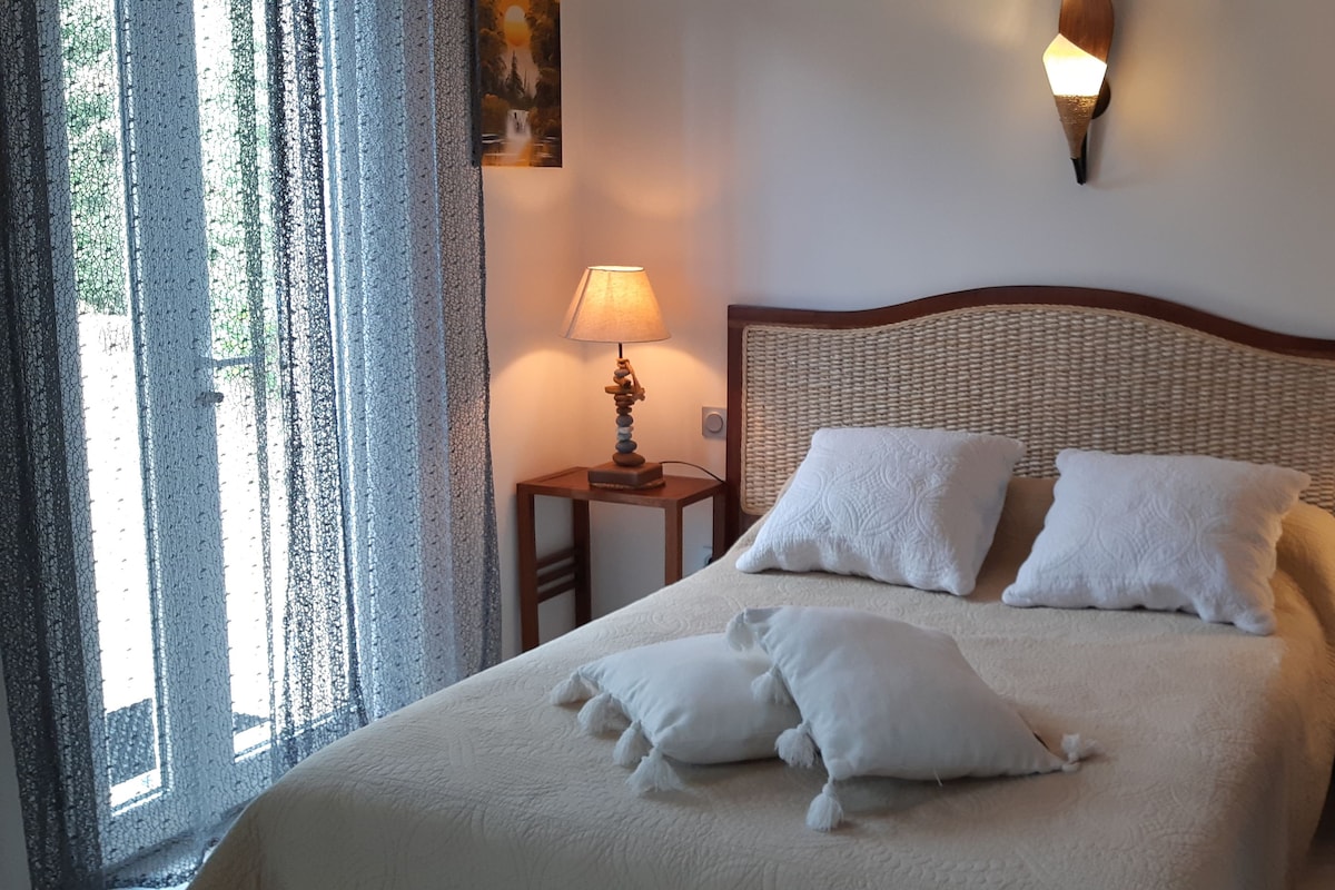Ett hotellrum med en stor säng, två sänglampor och utsikt över omgivningarna genom ett fönster med tunna, genomskinliga gardiner.