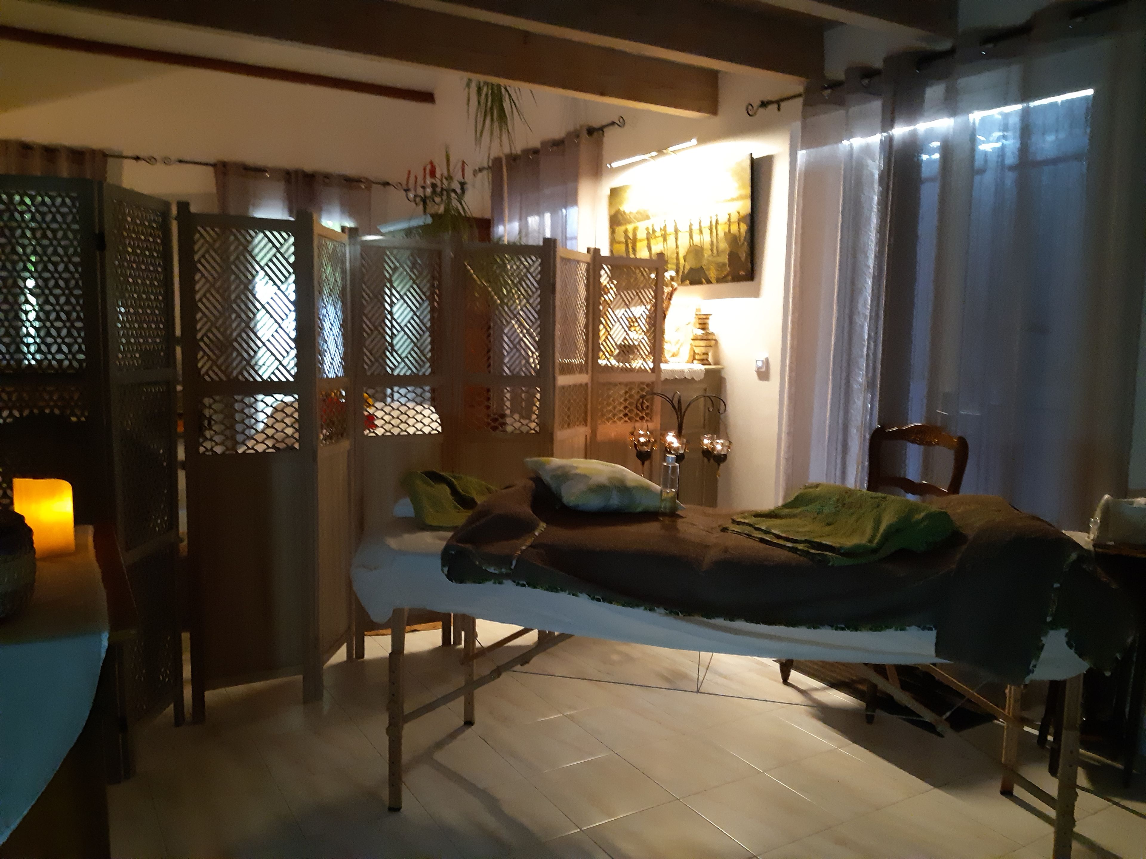 Ein Zimmer mit einem Bett, einem kleinen Tisch, einem Stuhl, einer Zimmerpflanze und einem an der Wand befestigten Regal mit Gegenständen.