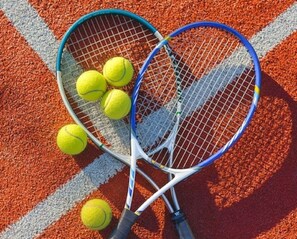 Två tennisracketar och tre tennisbollar på en röd och vit tennisbana.