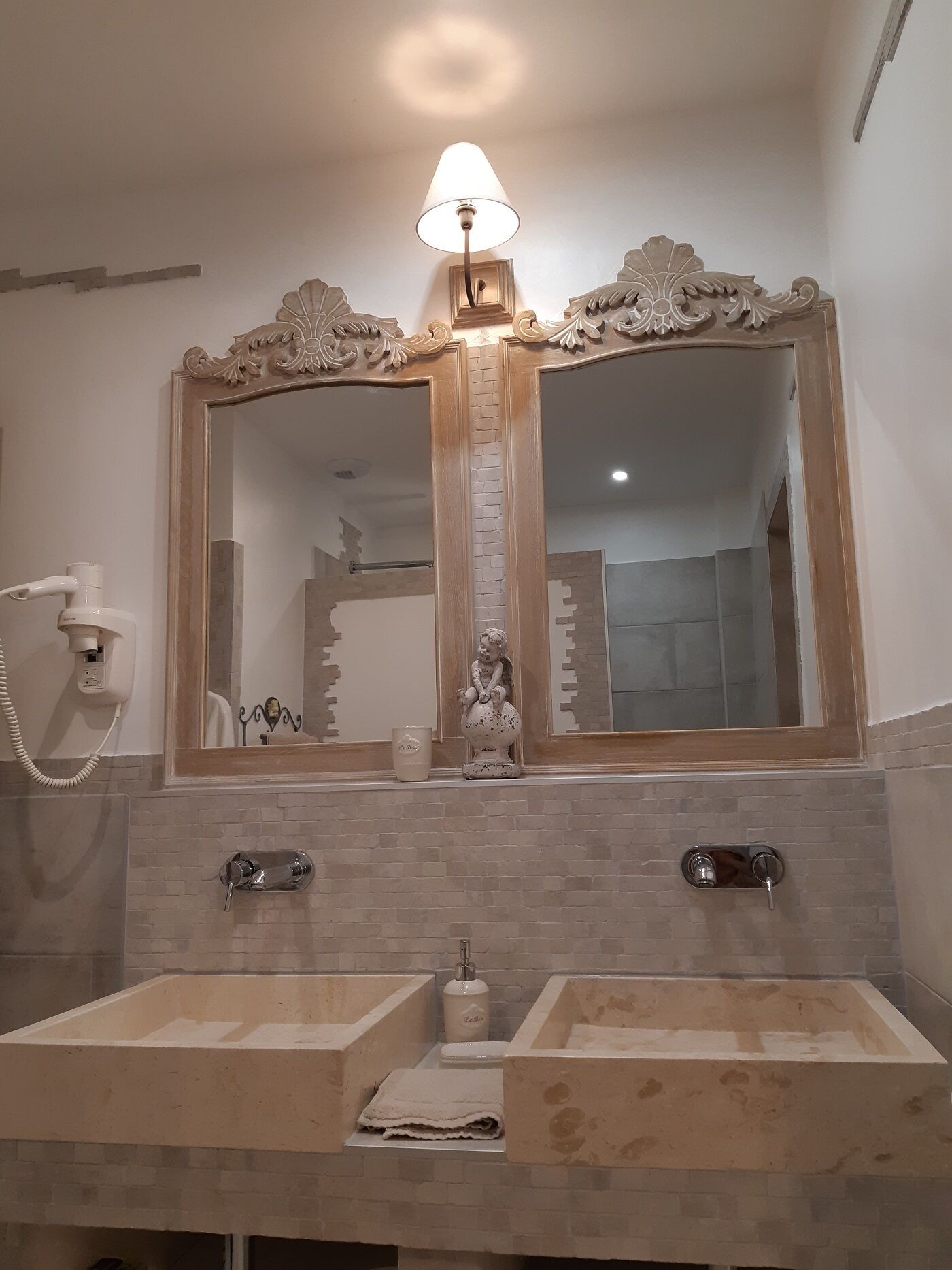 A bathroom with two sinks, a mirror, a wall-mounted phone, and a decorative statue.