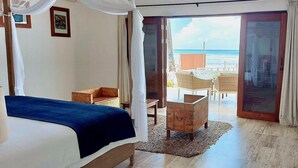 Une chambre à coucher avec un lit, une commode en bois, une petite table et une vue sur la plage par une porte ouverte.