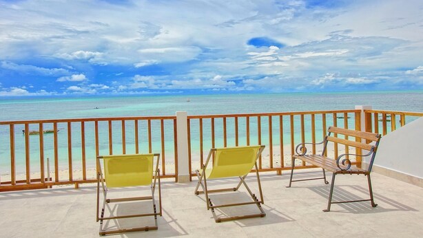 Un balcon avec deux chaises jaunes et un banc en bois, donnant sur une mer turquoise et un ciel dégagé.