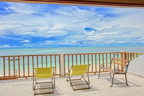 A balcony with two yellow chairs and a wooden bench, overlooking a turquoise sea and clear sky.
