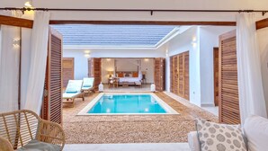 Un espace piscine offrant une vue dégagée sur la piscine, des chaises longues, ainsi qu’une chambre avec un lit et une table de chevet.