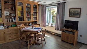 A cozy living room with a wooden dining table, chairs, a TV, and a bookshelf filled with books and decorative items. - Gerbers 1870 Chalet - A touch of Bavaria in Canada (Killaloe)