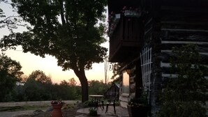 A rustic cabin with a stone exterior, a wooden deck, and a large tree in the foreground. - Gerbers 1870 Chalet - A touch of Bavaria in Canada (Killaloe)
