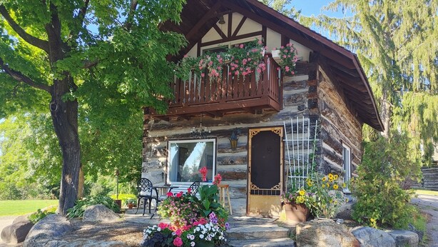 A rustic log cabin with a balcony adorned with flowers, a stone fireplace, and a large rock garden. - Gerbers 1870 Chalet - A touch of Bavaria in Canada (Killaloe)