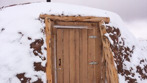 Een houten deur met metalen scharnieren en een metalen grendel, omgeven door sneeuw.