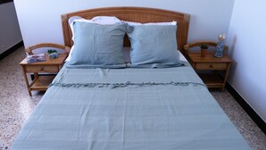 A neatly made bed with a light blue bedspread and pillows, flanked by wooden nightstands with small potted plants and decorative items. - Family house l'Ospedale - Porto-Vecchio (Porto-Vecchio)