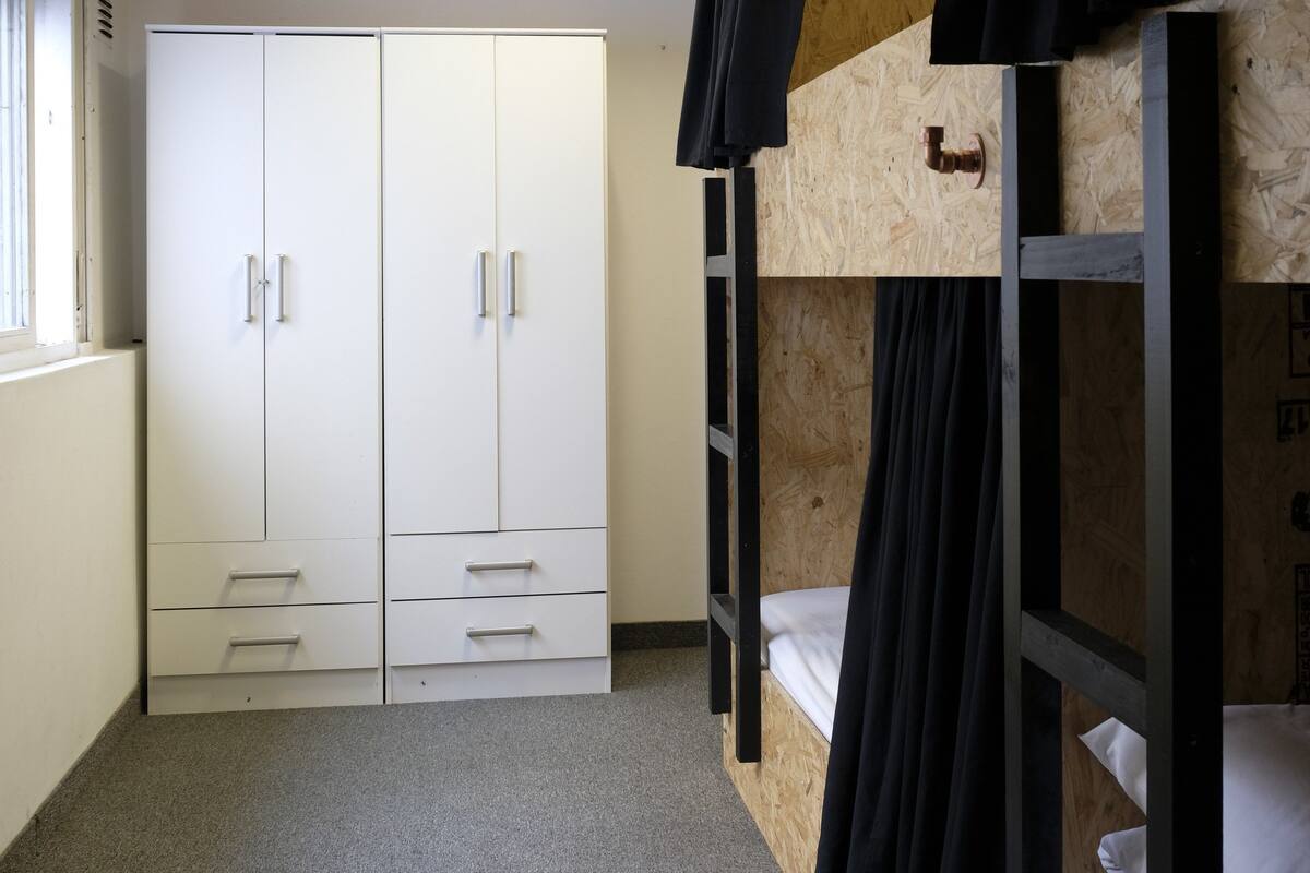 A dormitory room with bunk beds, a wardrobe, and a window.