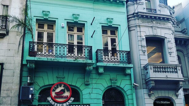 A green building with a restaurant sign, a MacStation store, and a Tango Box. - La Bamba Student Hostel (Buenos Aires)