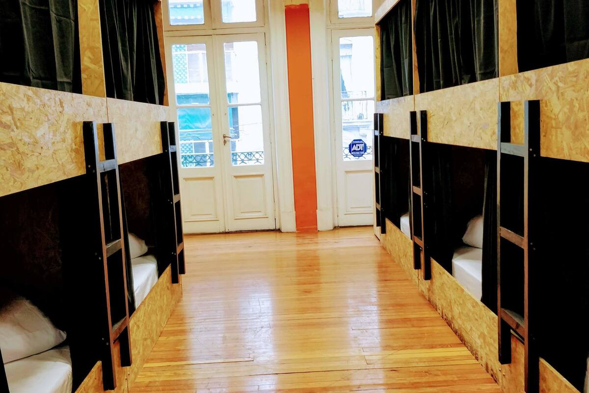 A corridor with bunk beds, wooden flooring, and a view of the outside through windows.