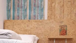 A room with a wooden bed frame, a small wooden shelf with a retro poster, and a patterned curtain. - La Bamba Student Hostel (Buenos Aires)