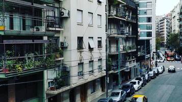 Um edifício residencial com várias andares, varandas, carros estacionados e uma rua desimpedida.