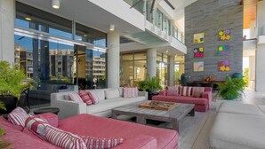 Un'ampia area interna con arredi moderni, tra cui divani e un tavolino da caffè, e ampie finestre che offrono vista sugli edifici circostanti.