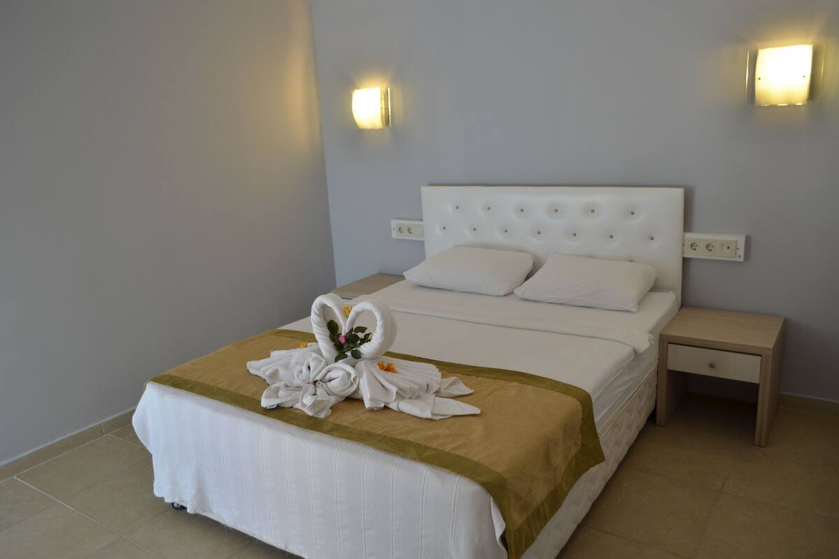 A neatly made bed with a white headboard, a gold accent at the foot, and a floral arrangement on the bedspread. There are two bedside tables with lamps, and the walls are painted light grey.