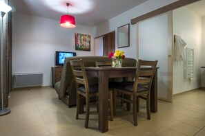 Un coin repas avec une table et des chaises en bois, un téléviseur, un luminaire suspendu rouge et un radiateur.