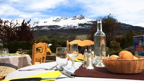 Een eettafel buiten, met uitzicht op bergen, zout- en peperstel, een fles en brood.