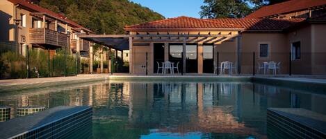 Una piscina con borde de azulejos, rodeada de edificios con balcones y una zona de estar cubierta.