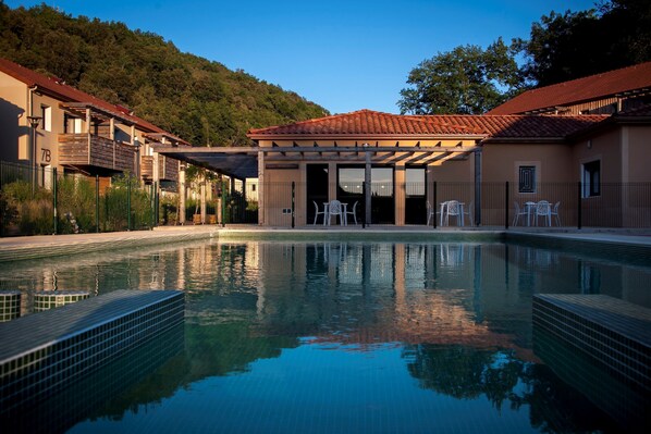 A swimming pool with a tiled edge, a covered seating area, and a building with balconies.