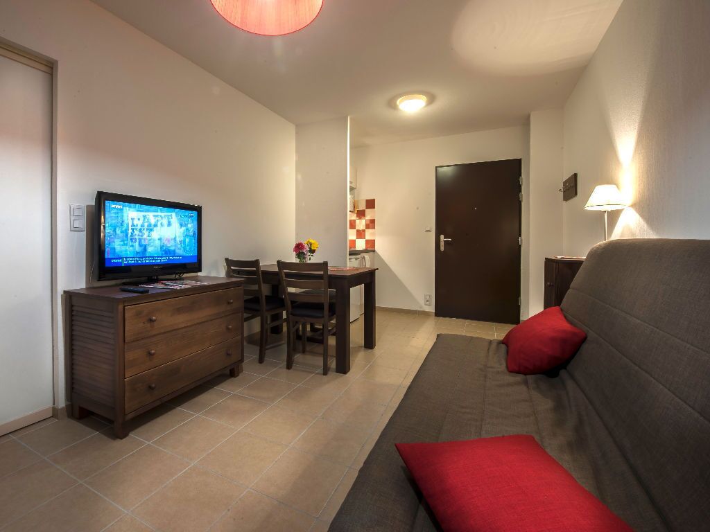 Ein Wohnzimmer mit Fernseher, einer Couch, einem Esstisch und einem Sessel.