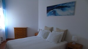 Een slaapkamer met een bed, een houten dressoir, een nachtkastje en een schilderij aan de muur.