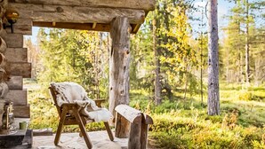 Tunnelmallinen, maalaishenkinen puumökki, jossa on kivinen kuisti, puinen tuoli ja penkki.