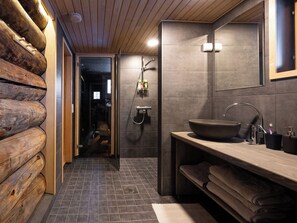 Een moderne badkamer met een wand van houten boomstammen, een ruime wastafel en een spiegel.