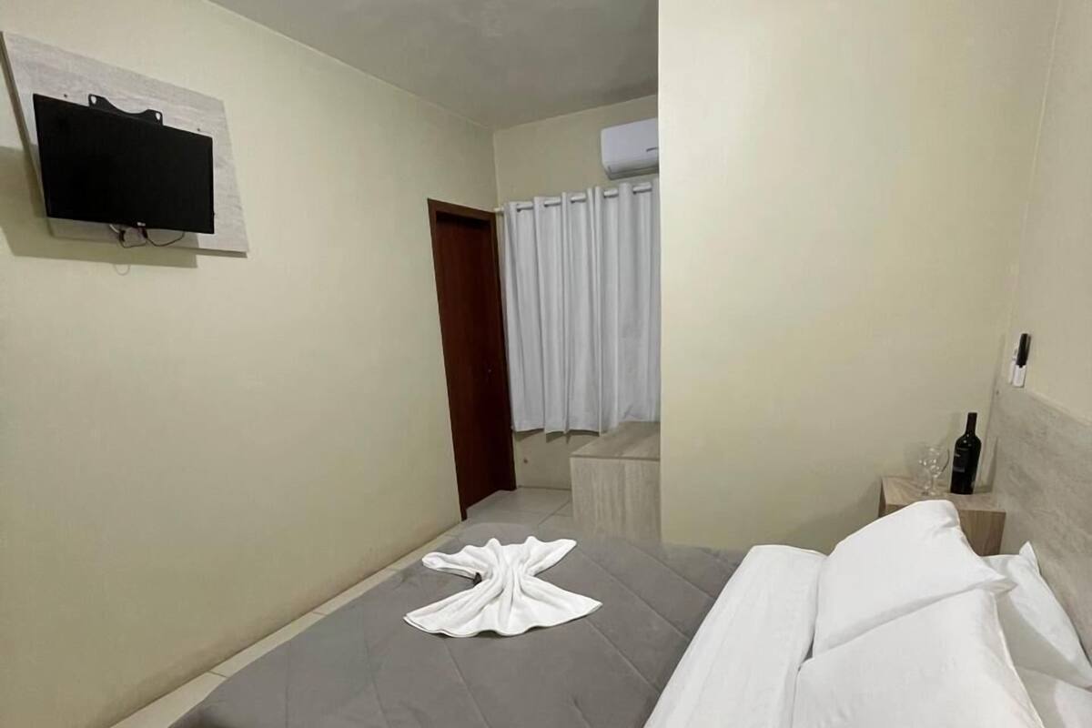 Une chambre d’hôtel avec un lit, un téléviseur à écran plat fixé au mur, une table de chevet en bois et une fenêtre avec des rideaux.
