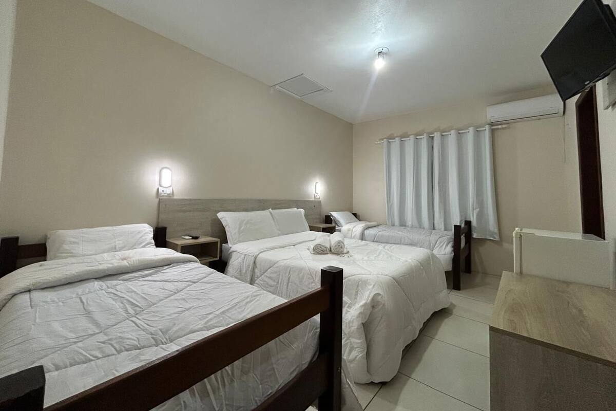 Une chambre d’hôtel avec trois lits, un téléviseur à écran plat fixé au mur et un luminaire au plafond.
